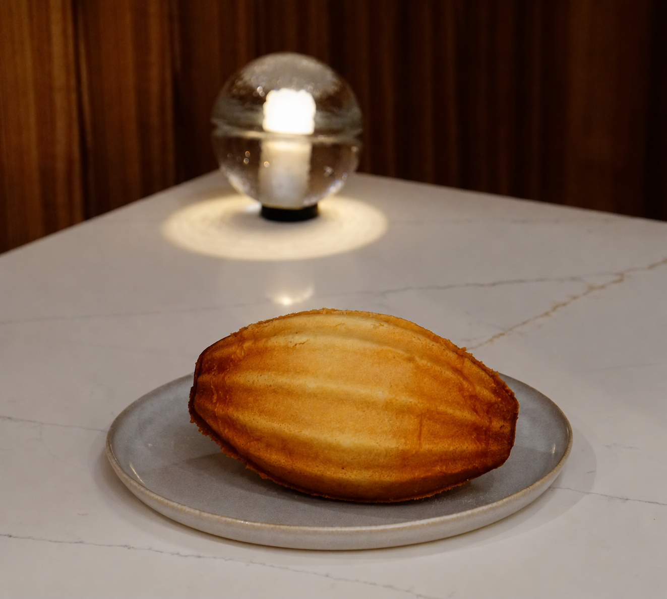 A golden oval bread on a ceramic plate at a softly lit bakery table